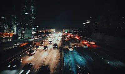 Avenida à noite com faróis de veículos em movimento